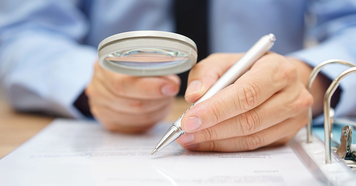 businessman is analyzing through magnifying glass contract and